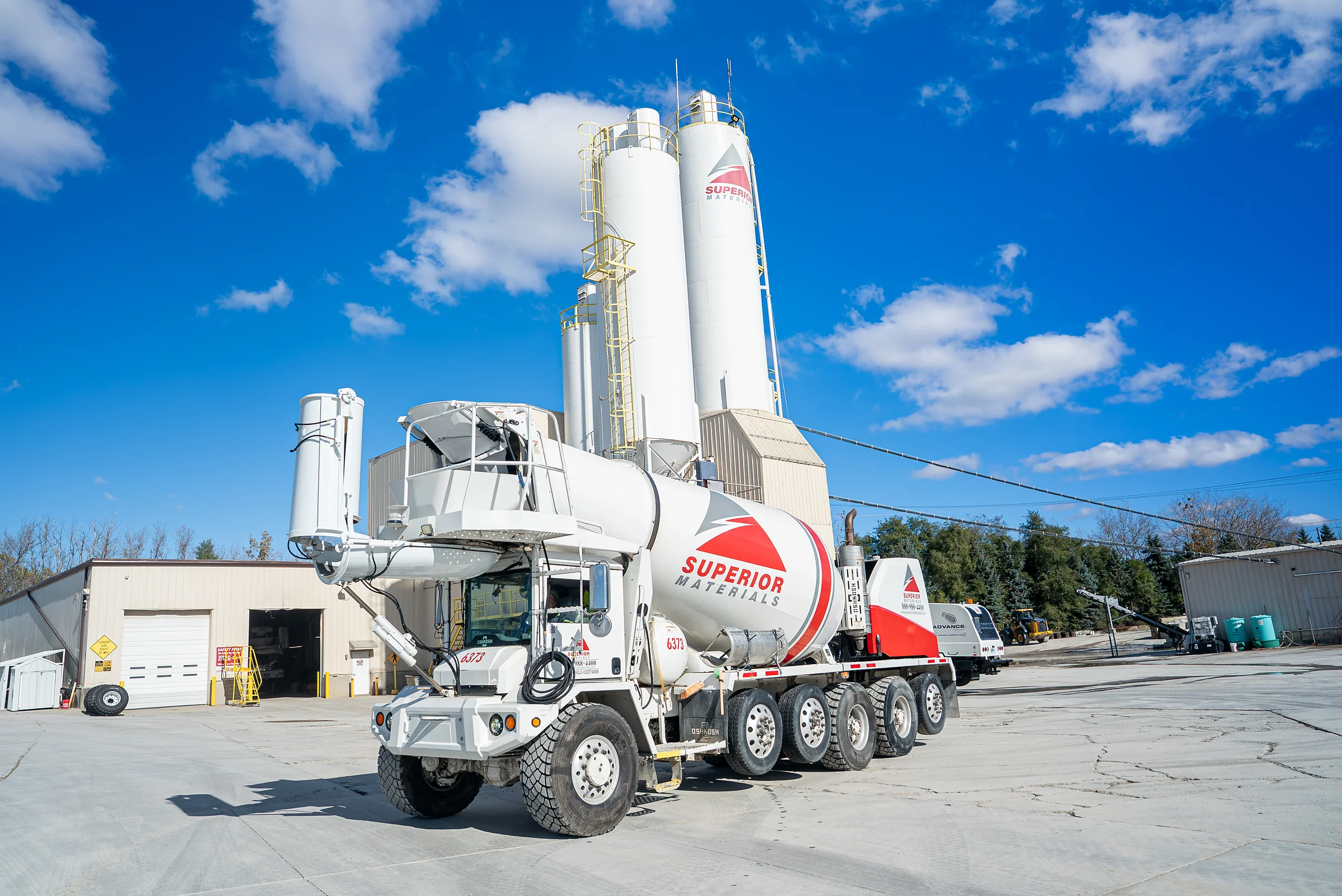 Superior Materials' Ready-mix Concrete - white front discharge mixer truck in front of cement silos at a plant